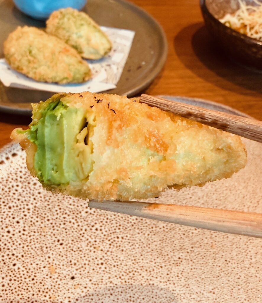 Half-eaten avocado katsu at Reif Dubai on chopsticks showing the crispy exterior and soft avocado inside.